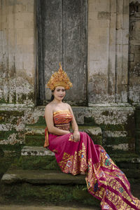 Portrait of young woman wearing traditional clothing sitting on steps against house