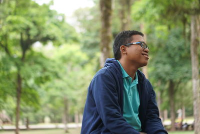 Young man looking away against trees