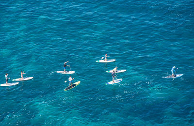 High angle view of people enjoying paddleboarding in sea on sunny day