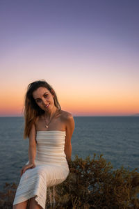 Young woman standing at beach against clear sky during sunset