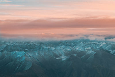 Aerial view of snowcapped mountains against cloudy sky at dusk 