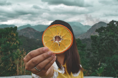 Woman holding slice of orange against mountains