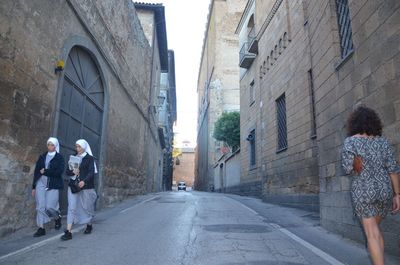 Rear view of people walking on road amidst buildings