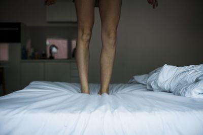 Low section of woman standing on bed at home