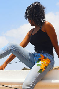 Rear view of woman looking down while sitting against sky