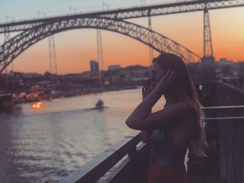 Side view of young woman standing on promenade by river against sky during sunset