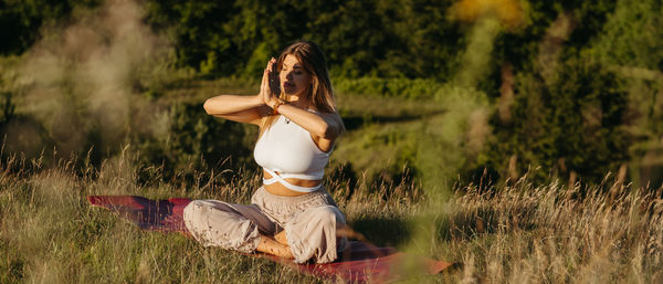Young woman practicing yoga and meditation on the mat outdoors at sunset with beautiful landscape