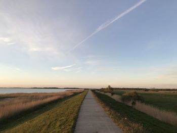 Road amidst field against sky during sunset