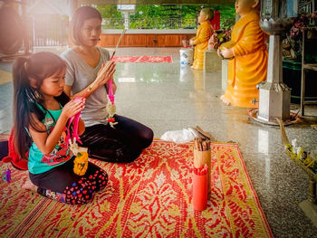 Side view of mother and daughter holding incense while praying in temple