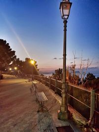 Street lights on road against sky during sunset