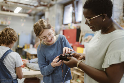 Smiling teacher and student examining electrical component in technology class at school