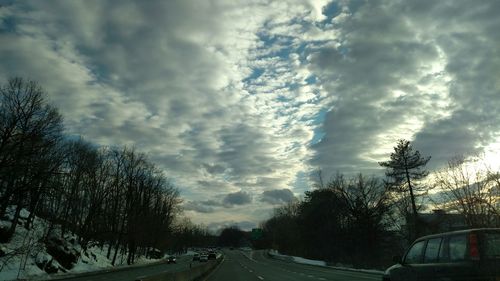 Road amidst trees against cloudy sky