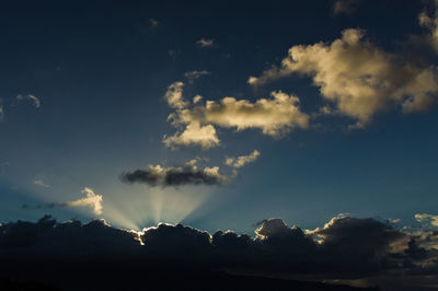 Low angle view of sunlight streaming through clouds