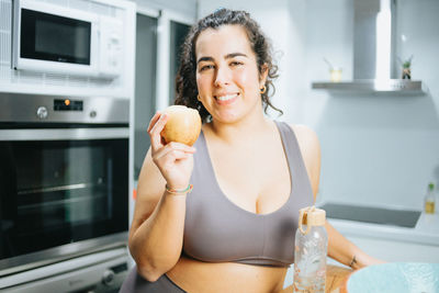 Portrait of young woman eating fruit at home