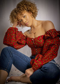 Young woman looking away while sitting against red wall
