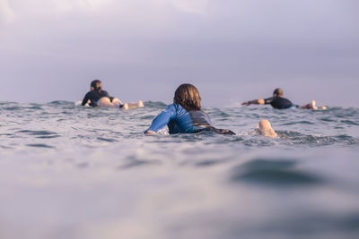 Rear view of friends surfing in sea against sky