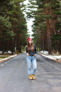 Happy young girl walking in the middle of lonely road in snowy forest.