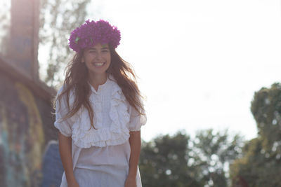 Cheerful woman wearing purple flowers while standing against clear sky