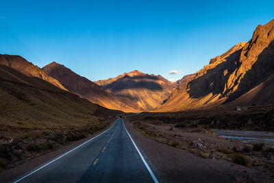 Road leading towards mountains against clear sky