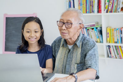 Granddaughter and grandfather using laptop at home