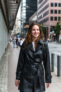Portrait of beautiful young woman standing on sidewalk in city