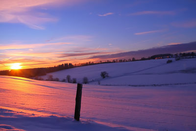 Scenic view of snow covered field against sky during sunset