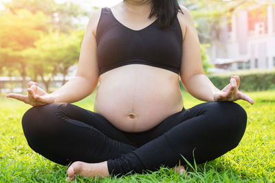 Low section of pregnant woman meditating in lotus position at park