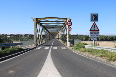 Road sign on bridge against clear blue sky