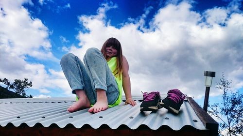 Portrait of woman sitting on roof against cloudy sky