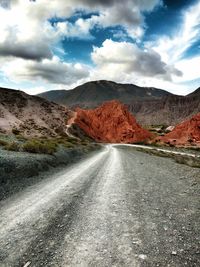 Dirt road leading towards mountains against sky