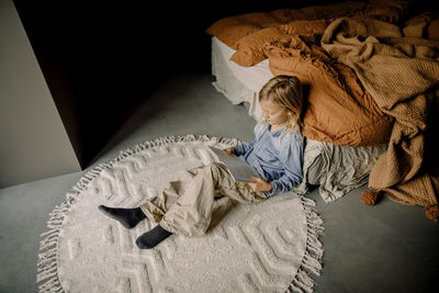 High angle view of boy reading book while sitting near bed in bedroom at home