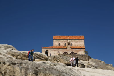 People on rock against clear blue sky