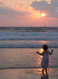 Rear view of baby girl at beach during sunset