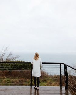 Rear view of woman looking at sea while standing by railing