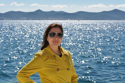 Portrait of smiling young woman standing by sea against sky