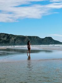 Rear view of woman standing at beach against sky