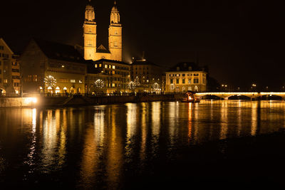 Illuminated buildings by river against sky at night