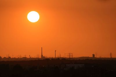 Silhouette of factory against orange sky