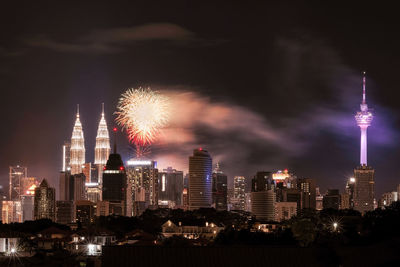 Firework display over illuminated buildings against sky at night