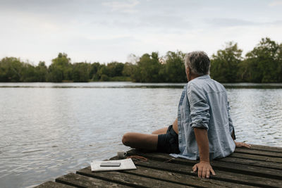 Senior man sitting on jetty at a lake
