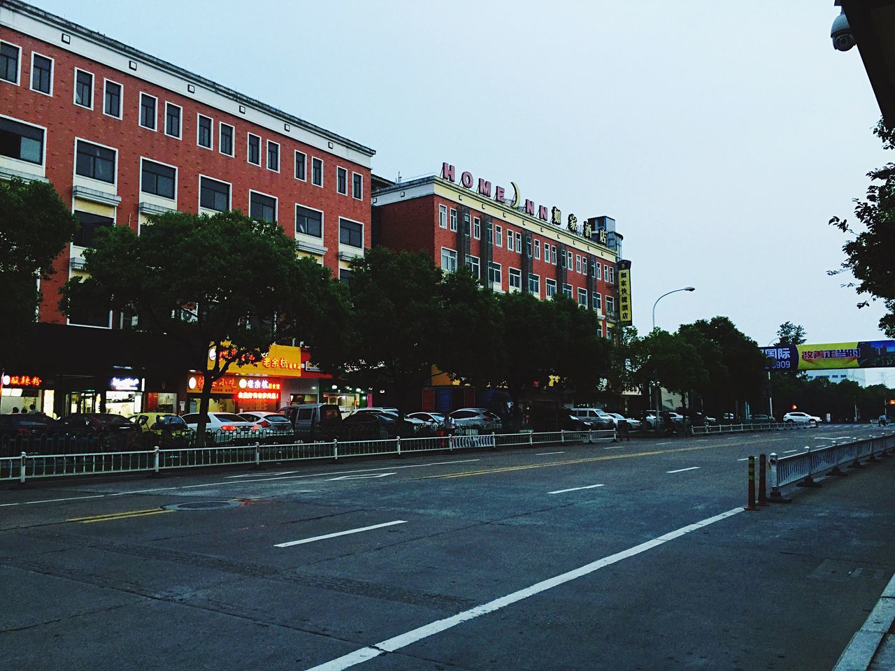 building exterior, architecture, built structure, clear sky, city, street, tree, road, incidental people, street light, building, city life, city street, transportation, outdoors, residential building, sky, residential structure, road marking, sidewalk