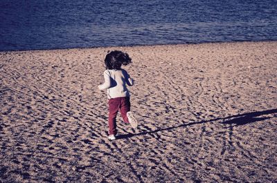 Rear view of girl running on sand at beach