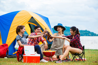 Friends holding beer bottle while sitting against sky