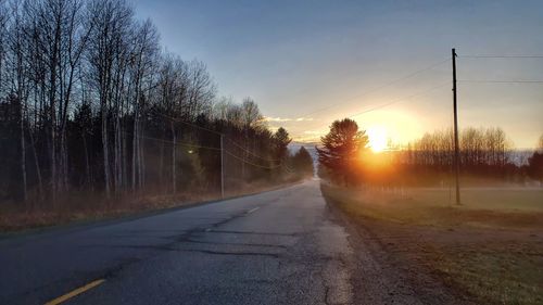 Road amidst trees against sky during sunset