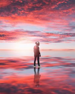 Rear view of man standing at beach against sky during sunset