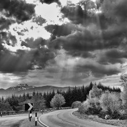 Empty road by trees against cloudy sky