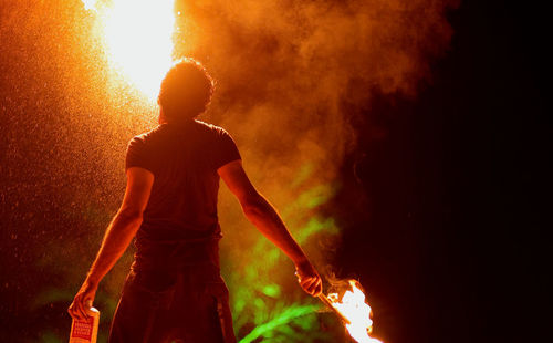 Rear view of man standing against fire at night