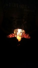 Close-up of hand holding illuminated candles in darkroom
