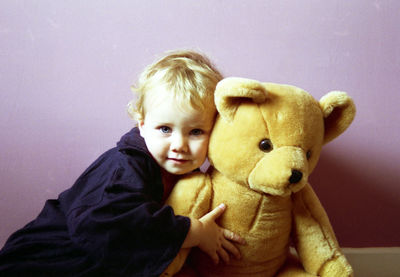 Portrait of toddler holding teddy bear sitting against wall