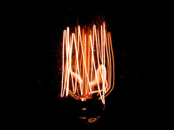 Close-up of illuminated light bulb against black background